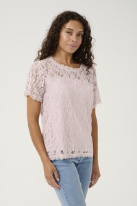 Top in pizzo di un rosa chiaro con maniche corte, scollatura e orlo a onde. Motivo floreale testurizzato e vestibilità ampia. Abbinato a jeans blu.