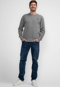 Felpa grigia con maniche lunghe, polsini e orlo a costine. Abbinata a jeans blu scuro e scarpe da ginnastica bianche. Dettaglio del logo semplice sul petto.