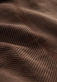 Tissu en velours côtelé marron avec des côtes verticales visibles et des plis doux créant des variations de lumière et d'ombre sur la surface.