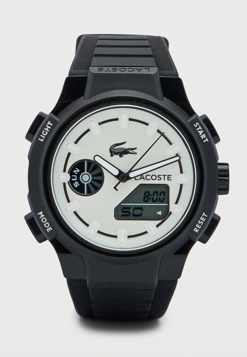 Μαύρο ψηφιακό ρολόι με στρογγυλό καντράν και λευκές λεπτομέρειες. Διαθέτει υφασμένο μαύρο λουράκι, λογότυπο και πολλαπλά κουμπιά λειτουργιών. Η οθόνη δείχνει την ώρα.