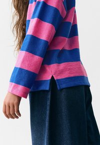 Randig skjorta med blå och rosa horisontella ränder, långa ärmar, rundad fåll och sidsluetter. Bärs med mörka jeans.