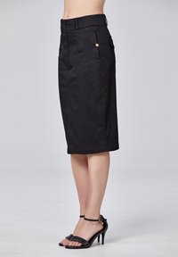 Jupe noire mi-longue en coton lisse, avec taille haute, deux poches latérales, un accent en bouton et une coupe ajustée.