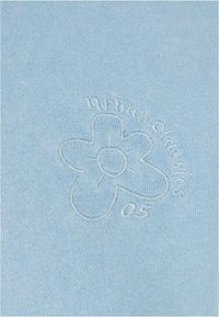 Šviesiai mėlynos spalvos tekstūruotas audinys, kuriame pavaizduota siuvinėta gėlių dekoracija ir subtiliai, kontrastinga siūle užrašas "urban classics 05".