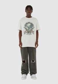 Hvitt bomull t-skjorte med et grafisk trykk og fet tekst. Kombinert med mørkegrå slitte jeans og hvite joggesko.