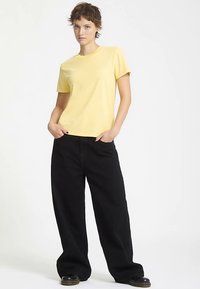 T-shirt gialla in cotone con collo rotondo, abbinata a pantaloni neri a gamba larga. L'outfit presenta una vestibilità comoda e un design minimale.