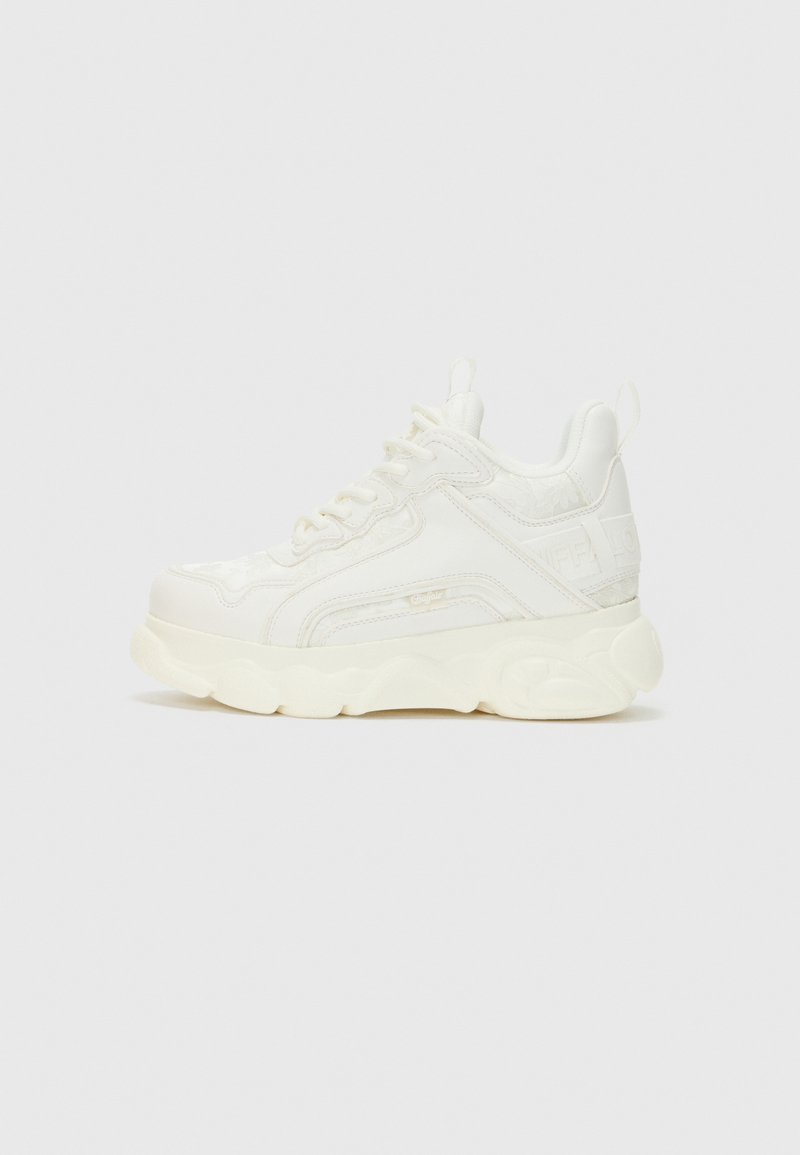 Sneaker blanc en matériau synthétique texturé, à semelle épaisse et design à lacets. Présente un logo subtil sur le côté et une pointe arrondie.