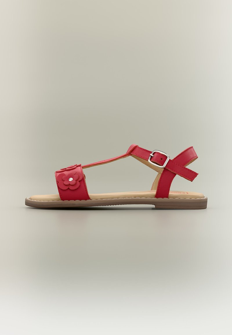 Κόκκινο επίπεδο σανδάλι με λουράκι αστραγάλου, αγκράφα και λουλουδένια διακόσμηση στο λουράκι των δακτύλων, παρουσιάζεται σε ουδέτερο φόντο.