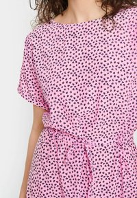 Rosa klänning med korta ärmar och rund halsringning, med ett litet blommönster i marinblått. Elastisk midja med knytband.