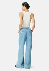 Top a canottiera bianca a coste e jeans a gamba larga blu chiaro, dotati di tasche posteriori e vita alta, progettati con una vestibilità rilassata e una morbida texture.