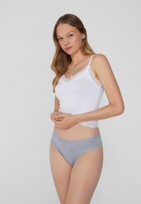 Camisole blanche avec des bordures en dentelle et des bretelles fines, associée à une petite culotte gris clair avec des accents en dentelle le long de la taille et des ouvertures des jambes.