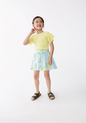 Top amarillo con relieve y mangas de lunares, combinado con una falda floral azul claro con limones. Lleva sandalias marrones.