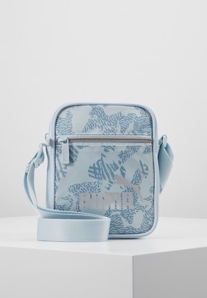 Petit sac bandoulière bleu clair avec motif abstrait, poche zippée sur le devant et logo Puma, posé sur une surface blanche.