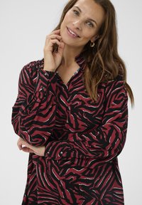 Red and black blouse featuring a bold zebra print, long sleeves with button cuffs, and a relaxed collar for a contemporary look.