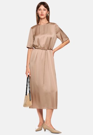 Midi dress in beige satin, with short sleeves, a cinched waist, and a straight silhouette. Paired with a small beige bag and pointed shoes.