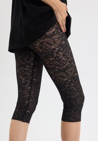 Svart blonde leggings med blomstermønster, tettsittende design og kort lengde, med teksturerte detaljer og elastisk midje.
