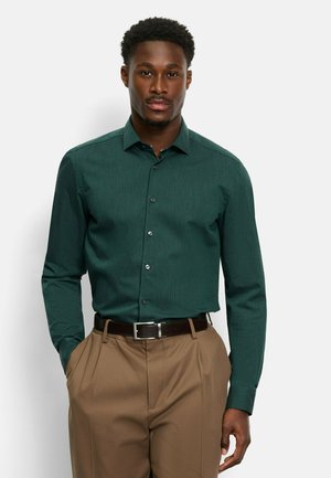 Dark green button-up shirt with a subtle texture, long sleeves, and a pointed collar, paired with light brown trousers and a brown belt.