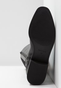 Bottine noire avec un motif matelassé, en cuir lisse, à talon bas et semelle en caoutchouc texturé, avec détails de taille.