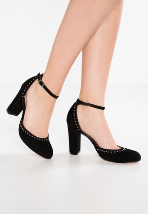 Black suede high-heeled shoes with an ankle strap. Features a rounded toe and decorative silver studs along the edge.