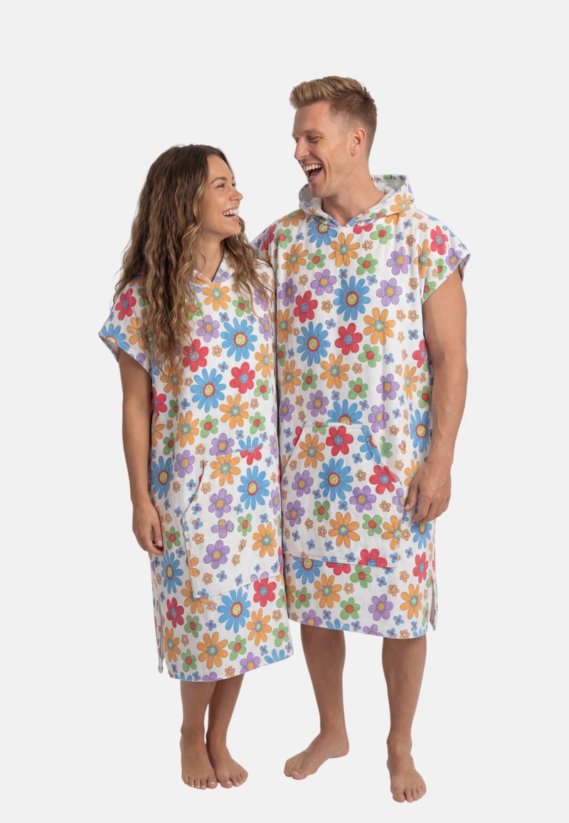 Een glimlachende man en vrouw staan op blote voeten en dragen bijpassende mouwloze gewaden met capuchon, kleurrijke bloemenprints en zakken aan de voorkant.