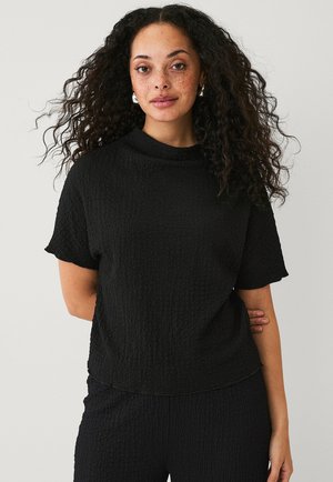 Schwarzes, strukturiertes Strickoberteil mit hohem Kragen und kurzen Ärmeln, das einen lockeren Schnitt hat. Der Stoff wirkt leicht und leicht zerknittert.