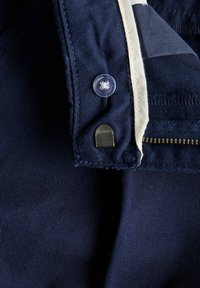 Jūras spēku audums ar ribotu tekstūru, kas ietver caurspīdīgu pogu, metāla aksesuārus un atklātu rāvējslēdzēju. Ietver kontrastējošas baltas šuves.