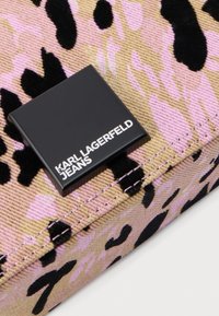 Közeli kép rózsaszín és bézs leopárdmintás anyagról fekete foltokkal, középen egy fekete négyzet alakú címkével, amelyen a "Karl Lagerfeld Jeans" felirat olvasható.
