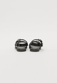 Svart sandaler med flere justerbare stropper og metallspenner. Flat såle med en teksturert fotseng. Minimalistisk design, ingen synlige mønstre.