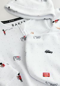 Vit bomullsbaby-outfit med små London-inspirerade illustrationer, inklusive en röd dubbeldäckare, svart taxi och vakter.