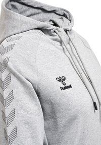 Felpa grigia con cappuccio regolabile, caratterizzata da motivi a zigzag neri sulle maniche e da un piccolo logo nero sul petto.