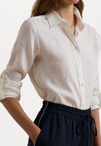 White linen shirt with a classic collar and button closure, featuring rolled-up sleeves. Paired with black joggers featuring an elastic waistband.
