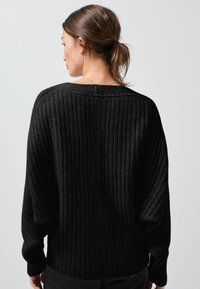 Schwarzer gerippter Pullover mit rundem Halsausschnitt, oversized Passform und langen Ärmeln. Das strukturiertes Material betont die vertikalen Linien und die leicht fallende Silhouette.