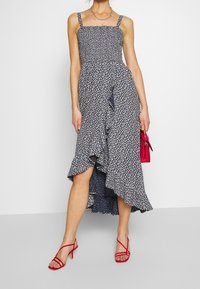 Marinblå blommig klänning med spaghettiband, volang nederkant och hög slits. Kombinerad med röda sandaler med band och en liten röd handväska.