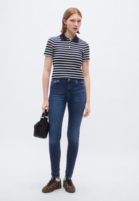 Tengeri kék és fehér csíkos galléros póló, testhezálló farmernadrág, fekete kis kézitáska és leopárdmintás cipők, amelyek laza öltözéket és modern stílust mutatnak be.