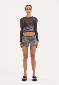 Schwarzes Mesh-Croptop mit langen Ärmeln, bedruckt mit grafischen Rosen und dem Text "LOVE HARD"; kombiniert mit einem bedruckten Minirock in verschiedenen Farben und Designs.