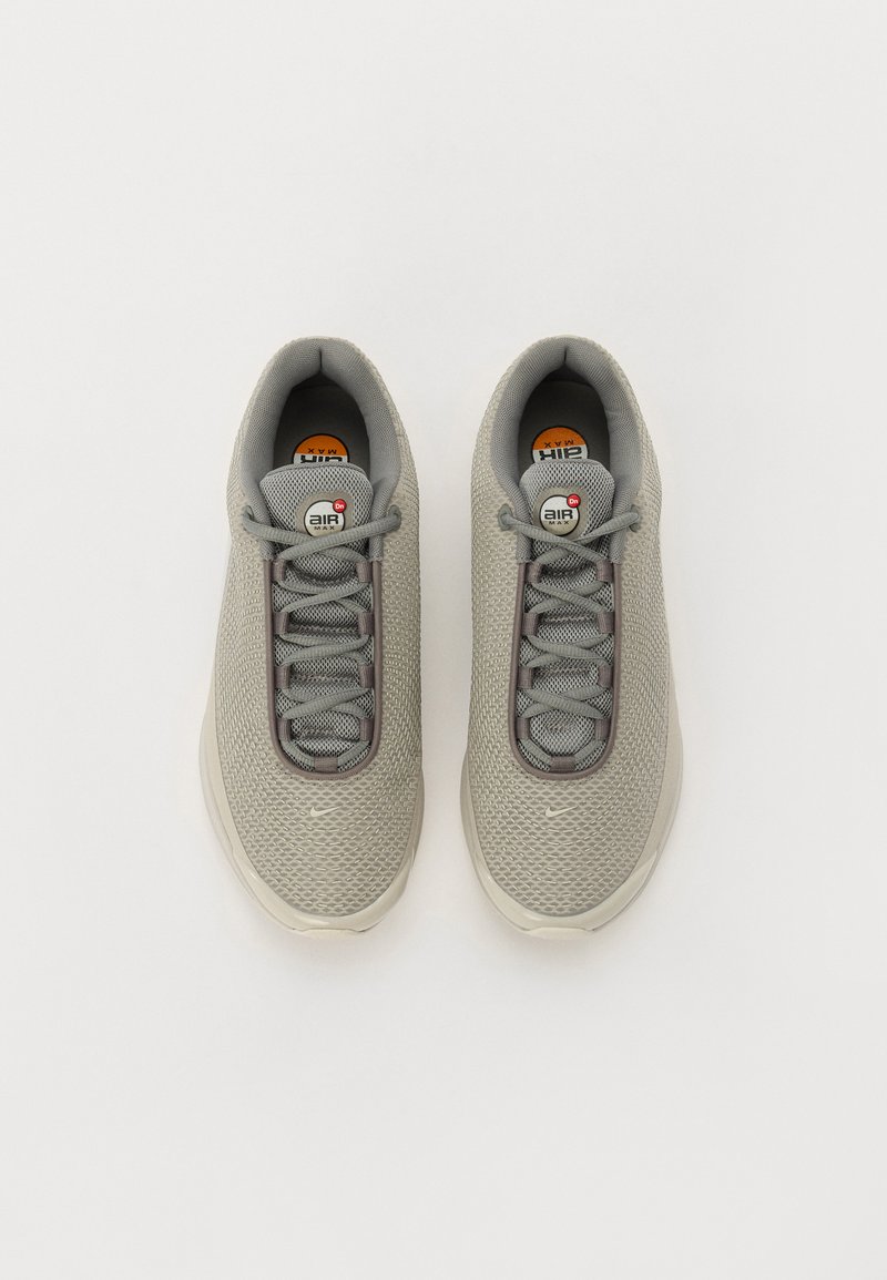 Zapatos deportivos grises con parte superior de malla, puntera redonda, cordones y detalles texturizados. Presenta la marca Air Max en la lengüeta. Diseño ligero.