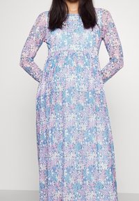 Sukienka z długim rękawem w kwiatowy wzór, wykonana z lekkiego materiału. Charakteryzuje się pastelowoniebieskim tłem z różowymi i białymi wzorami kwiatowymi oraz marszczonym pasem.