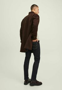 Sobretudo de lã castanho com um corte ajustado, bolsos laterais com aba, punhos com botão, combinado com jeans de denim escuro e sapatos de pele castanha.