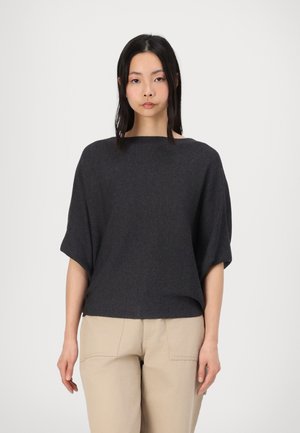 Dark gray, textured oversized top with a wide neckline, short sleeves, and a relaxed fit, paired with light beige trousers.