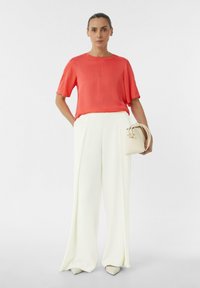 Koraalroze zijden blouse met korte mouwen, gecombineerd met hoge witte wijde broek. Een witte handtas en puntige beige hakken maken de look compleet.