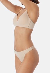 Stanik i bikini w kolorze nude. Stanik ma głęboki dekolt w kształcie litery V oraz regulowane ramiączka, podczas gdy bikini ma minimalistyczny krój.