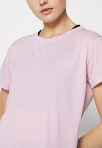 Camiseta deportiva de color rosa claro, de manga corta, con un escote redondo, hecha de un tejido transpirable, que presenta un pequeño logo en el área del pecho izquierdo.