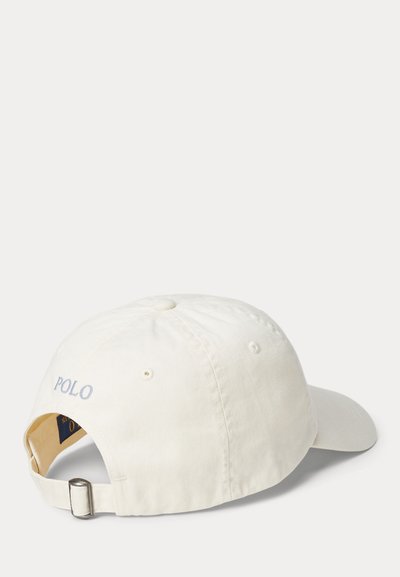 Hvid bomulds kasket med afrundet skygge og justerbar rem. "POLO" broderet i lyseblåt på bagsiden. Diskret tekstur, afslappet design.