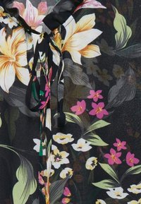 Svart blommig blus med stora gula och rosa blommor, gröna blad och en knytning vid halsen. Tillverkad av lätt, texturerad tyg.