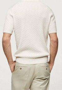 Bílý krátký rukáv pletený svetr s texturovaným vzorem, kulatým výstřihem a žebrovaným lemem. Kombinován s lehce béžovými kalhotami na míru.