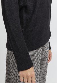 Melnā adītā džemperis ar struktūru audumu. Ar garām, pieguļošām piedurknēm un taisnu apakšmalu. Apvienots ar rūtainu svārku.