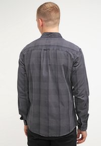 Koszula z długim rękawem w ciemnoszarym kolorze z kratkowanym wzorem. Posiada kołnierzyk zapinany na guziki oraz lekko zaokrąglony dół. Wykonana z miękkiej mieszanki bawełny.