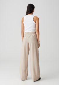 Pantalons larges beiges avec une taille élastique haute. Texture lisse avec des poches latérales et une poche arrière unique. Pas de motifs visibles.