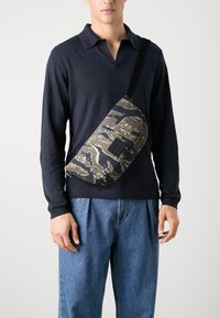 Borsa a tracolla con un motivo camouflage in tonalità blu scuro e oliva, realizzata in tessuto leggero, con un patch logo in hardware nero.