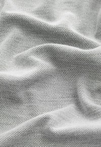 Tissu gris clair texturé avec un motif géométrique subtil, présentant des plis doux et froissés ainsi qu'une finition de surface lisse.