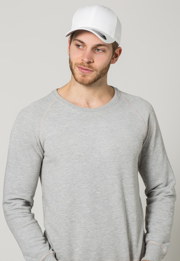 Grijze sweatshirt met raglanmouwen, lichte stikselaccenten en een ronde halslijn. Gecombineerd met een effen witte pet.